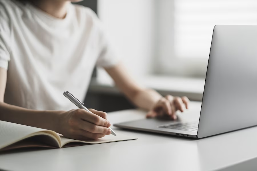 Woman using a pen to write in front of a laptop